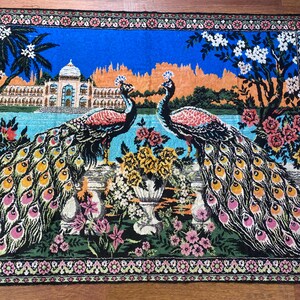 Peut inclure: Tapisserie d&eacute;corative repr&eacute;sentant deux paons aux plumes vibrantes, debout sur un mur surplombant un plan d'eau. L'arri&egrave;re-plan comprend un palais, des arbres et des fleurs, avec un ciel bleu et une bordure florale.