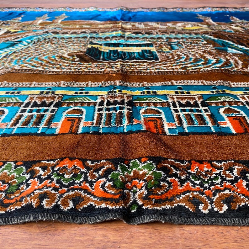May include: A detailed, colorful prayer rug with a central architectural design, featuring shades of brown, blue, and orange. The rug has a patterned border with floral and geometric elements.