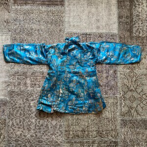 Puede incluir: Una chaqueta de brocado azul y dorado con cuello mandar&iacute;n y mangas largas. La chaqueta est&aacute; decorada con un patr&oacute;n floral.