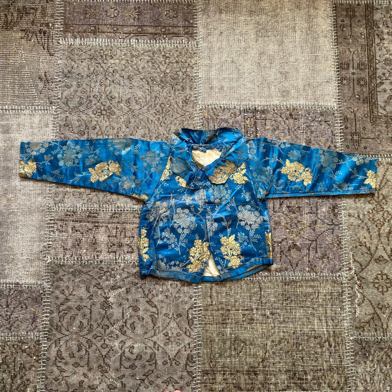 May include: A blue and gold brocade jacket with a mandarin collar and floral pattern.