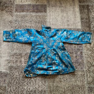 Puede incluir: Una chaqueta de brocado azul y plata con cuello alto y mangas largas. La chaqueta tiene un patr&oacute;n floral y est&aacute; hecha de una tela sedosa.