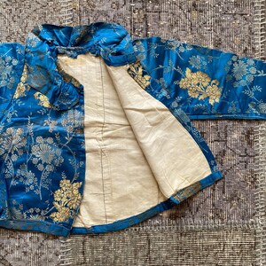 May include: A blue silk jacket with a gold floral pattern. The jacket is lined with a white fabric and has a mandarin collar.