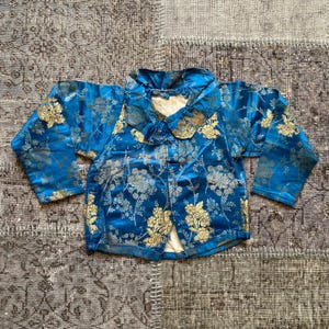 May include: A blue and gold brocade jacket with a mandarin collar and long sleeves. The jacket is decorated with a floral pattern.