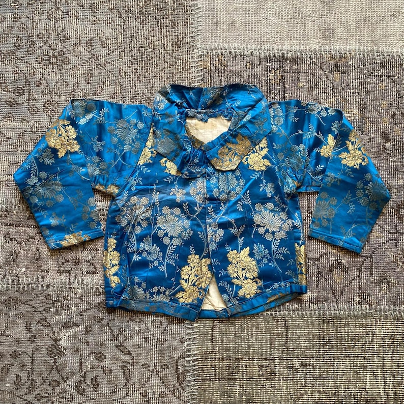 May include: A blue and gold brocade jacket with a mandarin collar and long sleeves. The jacket is decorated with a floral pattern.