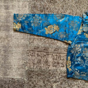 May include: A blue and gold brocade fabric with a floral pattern. The fabric is soft and luxurious, and it would be perfect for a variety of projects, such as clothing, upholstery, or home decor.