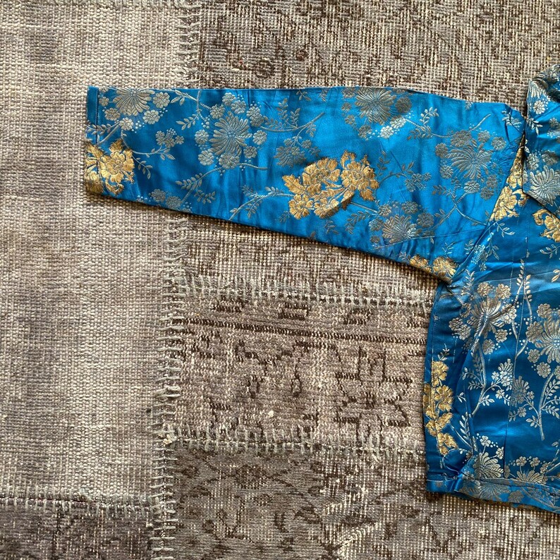 May include: A blue and gold brocade fabric with a floral pattern. The fabric is soft and luxurious, and it would be perfect for a variety of projects, such as clothing, upholstery, or home decor.