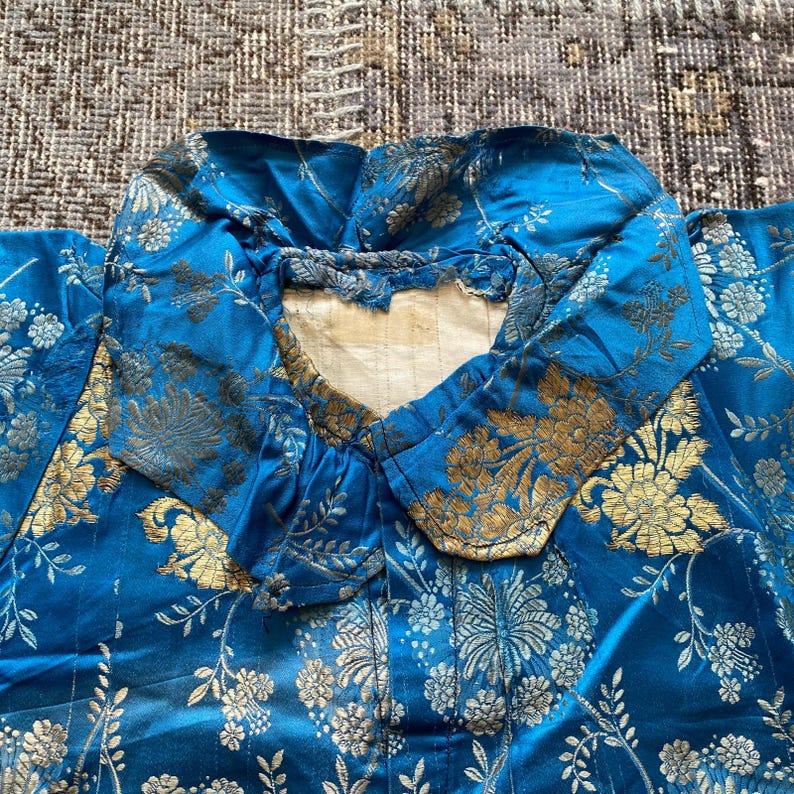 May include: A blue silk robe with a gold floral pattern. The robe has a large collar and is made of a luxurious fabric.