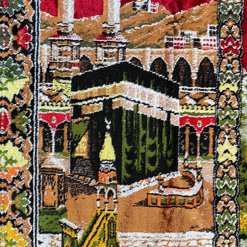 May include: A detailed prayer rug with a central depiction of the Kaaba in Mecca. The rug features a complex design with architectural elements, including minarets and arches, in shades of green, brown, red, and gold.