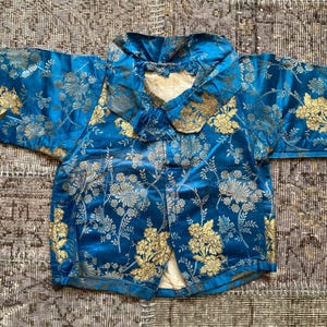 May include: A blue silk jacket with a gold floral pattern and a large collar. The jacket has a button closure and is in good condition.