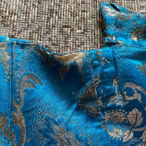 Puede incluir: Primer plano de una tela azul con un patr&oacute;n dorado. La tela tiene un aspecto texturizado, tejido y probablemente se utiliza para ropa o tapicer&iacute;a.