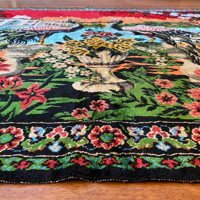 May include: A close-up of a vibrant rug with a floral and bird design. The rug has a black background with green, red, and blue floral patterns. A large vase of yellow flowers is in the center, with birds on either side.