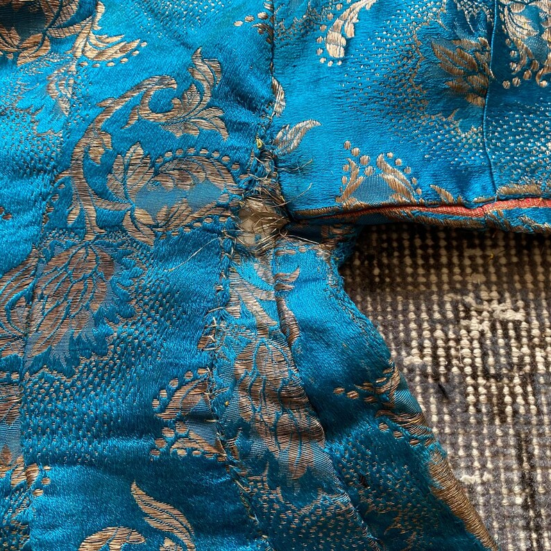 Puede incluir: Primer plano de una tela azul turquesa con un patr&oacute;n floral dorado. La tela tiene un borde deshilachado y est&aacute; ligeramente arrugada.