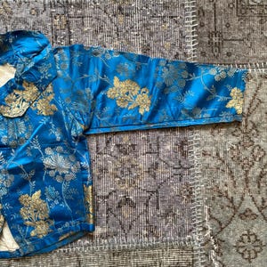 May include: A blue brocade jacket with gold floral embroidery. The jacket has a mandarin collar and long sleeves.