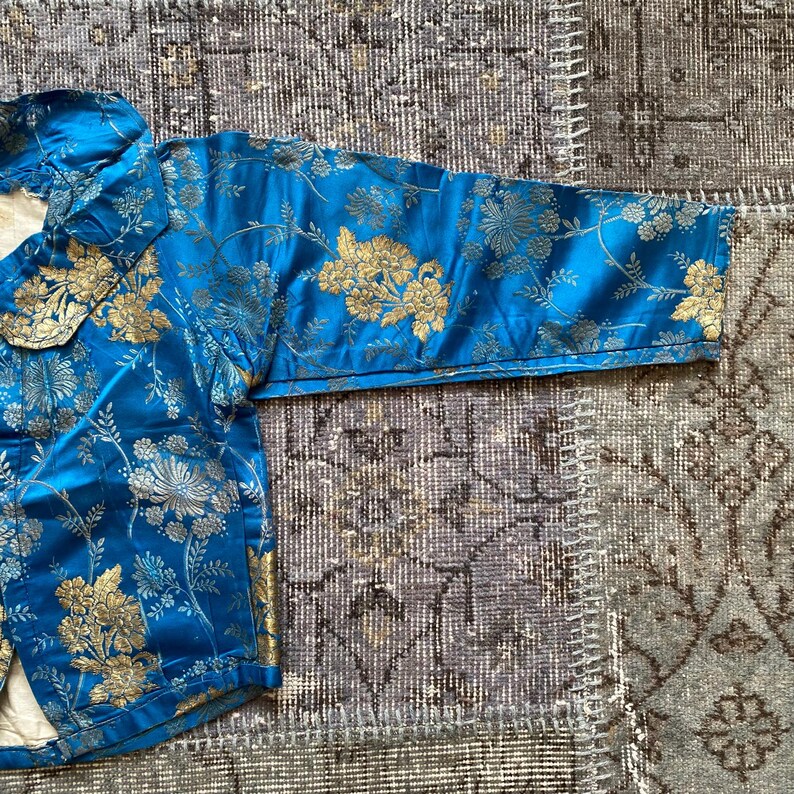 May include: A blue brocade jacket with gold floral embroidery. The jacket has a mandarin collar and long sleeves.