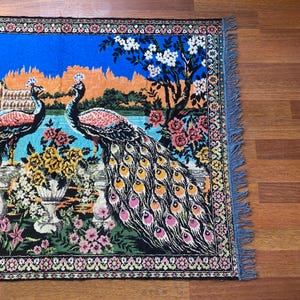 Peut inclure: Tapis d&eacute;coratif avec un motif de paon. Le tapis pr&eacute;sente deux paons avec un plumage d&eacute;taill&eacute;, sur fond de ciel bleu et d'&eacute;l&eacute;ments floraux. Le tapis a une bordure d&eacute;taill&eacute;e et des bords frang&eacute;s.
