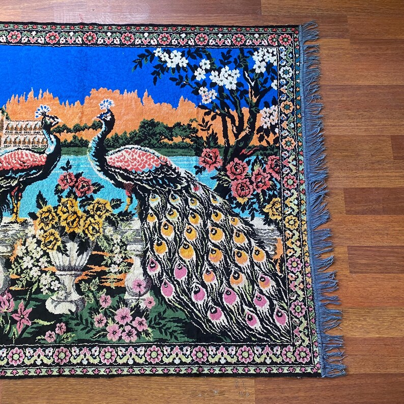 Peut inclure: Tapis d&eacute;coratif avec un motif de paon. Le tapis pr&eacute;sente deux paons avec un plumage d&eacute;taill&eacute;, sur fond de ciel bleu et d'&eacute;l&eacute;ments floraux. Le tapis a une bordure d&eacute;taill&eacute;e et des bords frang&eacute;s.