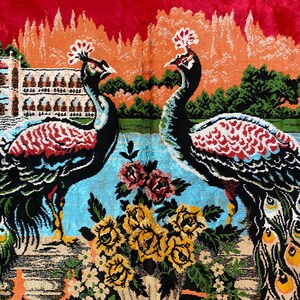 May include: A vibrant textile depicting two peacocks with detailed feathers, set against a landscape with a building, water, and flowers. The peacocks are black, red, and blue, with yellow and red accents.