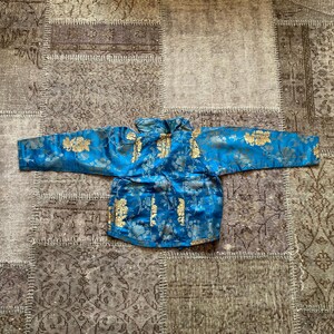 May include: A blue silk jacket with gold floral embroidery. The jacket has a mandarin collar and long sleeves.