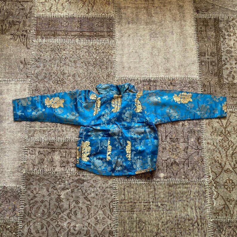 May include: A blue silk jacket with gold floral embroidery. The jacket has a mandarin collar and long sleeves.