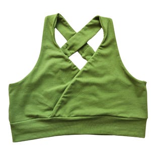 Könnte beinhalten: Ein grüner Sport-BH mit gekreuztem Rückendesign. Der BH besteht aus einem weichen, dehnbaren Stoff und hat ein breites Band am unteren Saum für Halt. Die Farbe ist ein leuchtendes, einfarbiges Grün.