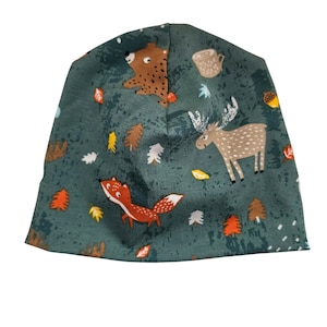 May include: A teal beanie hat with a forest animal print. The pattern includes a brown bear, a fox, a moose, trees, leaves, and a coffee mug. The hat is made of a soft, flexible material.