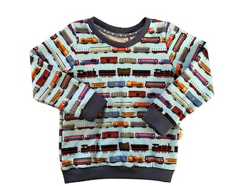 May include: A light blue long-sleeved sweatshirt with a repeating pattern of colorful toy trains on a white background. The sweatshirt has a navy blue ribbed crew neck and cuffs.