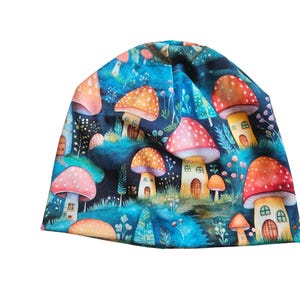 Può includere: Un berretto blu scuro con un fantasioso motivo a casette a forma di fungo. I funghi hanno cappelli rossi, arancioni e rosa con pois bianchi. Lo sfondo presenta una scena di foresta con alberi e piccole case.
