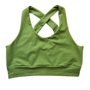 Peut inclure: Soutien-gorge de sport vert uni avec un dos croisé. Le soutien-gorge présente une large bande en bas et une encolure arrondie. Le tissu semble être une matière douce et extensible, adaptée aux activités sportives.
