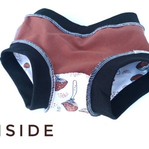 Pode incluir: Roupa interior com um painel de cor ferrugem s&oacute;lida, faixas el&aacute;sticas pretas na cintura e nas pernas com costuras brancas vis&iacute;veis, e um forro interior branco com um padr&atilde;o de ilustra&ccedil;&otilde;es de cogumelos castanhos. A palavra INSIDE est&aacute; impressa em castanho.