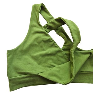 K&ouml;nnte beinhalten: Ein gr&uuml;ner Sport-BH mit einem einzigartigen Kreuzgurt-Design. Der BH besteht aus einem weichen, dehnbaren Stoff und hat ein breites Band am unteren Saum f&uuml;r Halt. Die Farbe ist ein lebendiges, erdiges Gr&uuml;n.