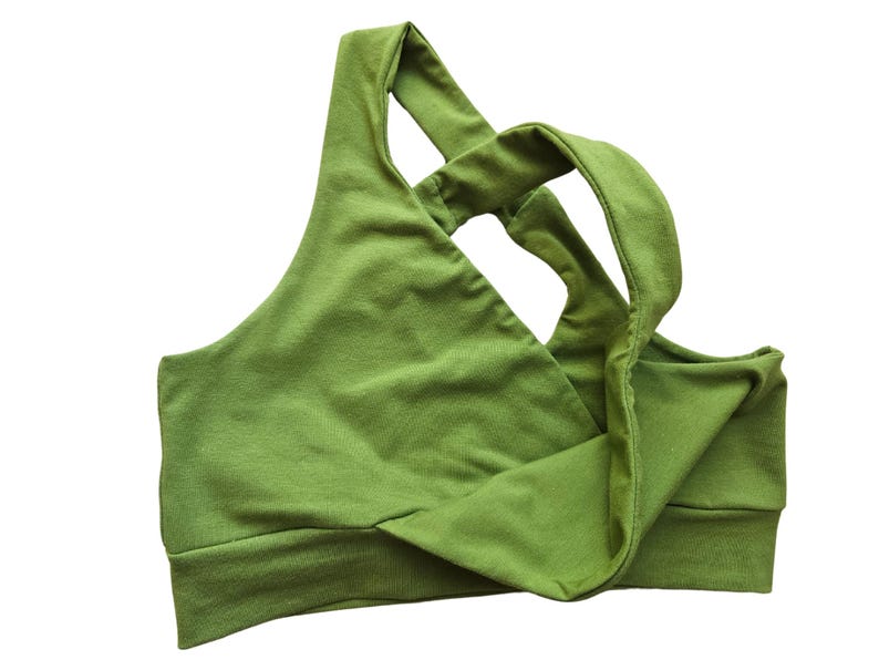 K&ouml;nnte beinhalten: Ein gr&uuml;ner Sport-BH mit einem einzigartigen Kreuzgurt-Design. Der BH besteht aus einem weichen, dehnbaren Stoff und hat ein breites Band am unteren Saum f&uuml;r Halt. Die Farbe ist ein lebendiges, erdiges Gr&uuml;n.