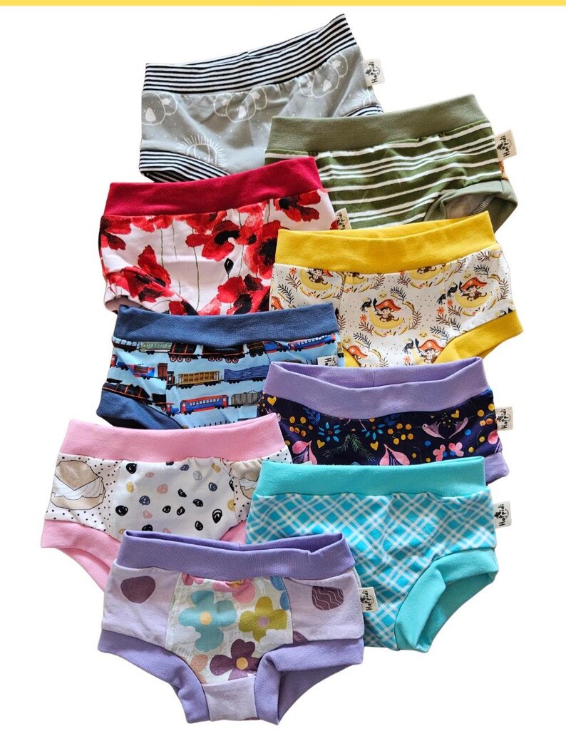 Pode incluir: Uma cole&ccedil;&atilde;o de nove pares de roupa interior infantil com v&aacute;rios padr&otilde;es, incluindo coalas, riscas verdes, papoilas vermelhas, faixas amarelas, comboios, motivos florais, pintas, xadrez azul e flores coloridas, cada uma com uma pequena etiqueta.