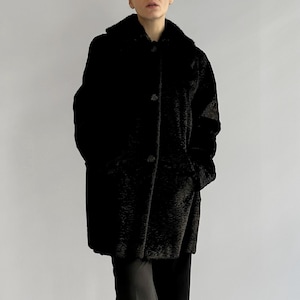 Könnte beinhalten: Ein schwarzer Kunstpelzmantel mit Knopfleiste und Kragen. Der Mantel wird von einer Person mit schwarzer Hose getragen.