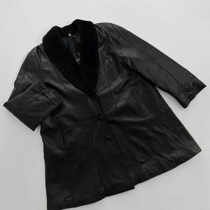 May include: Black leather coat with a faux fur collar. The coat has a button-up front, two front pockets, and long sleeves. The coat is a classic style, suitable for cooler weather.