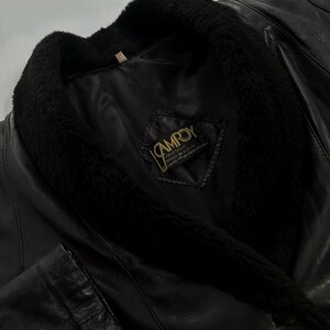 May include: Black leather jacket with a plush, black fur collar. The jacket features a label with the brand name "CAMROY". The leather appears to be smooth and the overall design is classic and timeless.