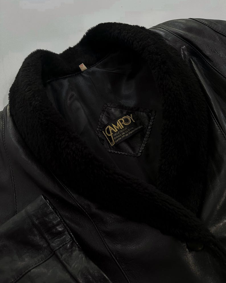May include: Black leather jacket with a plush, black fur collar. The jacket features a label with the brand name "CAMROY". The leather appears to be smooth and the overall design is classic and timeless.