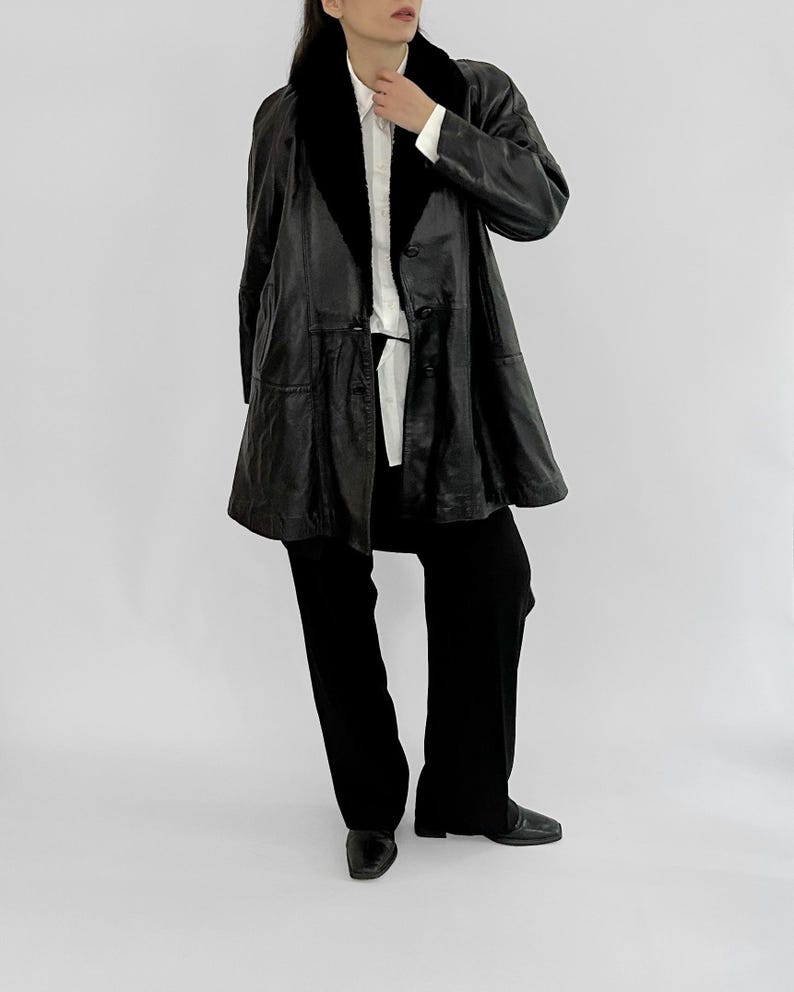 May include: A black leather coat with a black fur collar and a button-down front. The coat is paired with black pants and black shoes. The outfit is set against a plain white background.