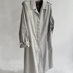 May include: A light gray trench coat with a plaid lining. The coat has a belt and a button closure.