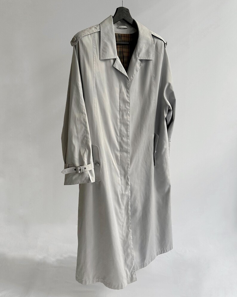May include: A light gray trench coat with a plaid lining. The coat has a belt and a button closure.