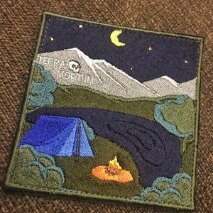 Puede incluir: Parche bordado con una escena de campamento nocturno. Una tienda de campaña azul está instalada bajo un cielo azul oscuro con una luna creciente y estrellas. El texto "TERRA MORTUM" es visible en el fondo.