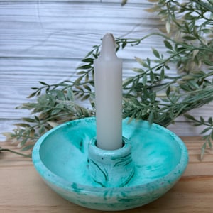 Op de afbeelding: Een teal en wit gemarmerde kandelaar met een witte kaars. De kandelaar heeft een ronde basis en een centrale kolom om de kaars vast te houden. De kaars is wit en cilindrisch. Decoratieve woondecoratie.