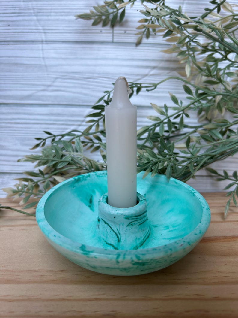 Op de afbeelding: Een teal en wit gemarmerde kandelaar met een witte kaars. De kandelaar heeft een ronde basis en een centrale kolom om de kaars vast te houden. De kaars is wit en cilindrisch. Decoratieve woondecoratie.