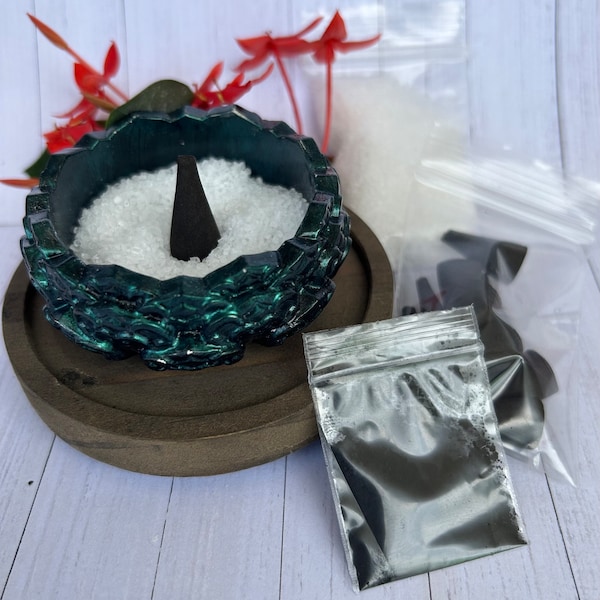 May include: A green ceramic incense burner with a black incense cone on a wooden base. There are three small bags of incense next to the burner.