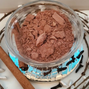 May include: A small glass bowl filled with a brown powder, a cinnamon stick, and cloves. The bowl is sitting on a silver tray with a blue and white design.