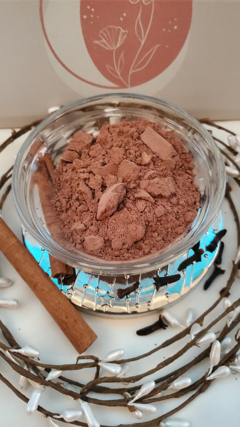 May include: A small glass bowl filled with a brown powder, a cinnamon stick, and cloves. The bowl is sitting on a silver tray with a blue and white design.
