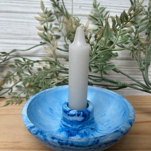 Op de afbeelding: Een blauw-witte gemarmerde kandelaar met een witte kaars. De kandelaar heeft een cirkelvormige basis en een centrale kolom om de kaars vast te houden. De kaars is wit en cilindrisch. Decoratieve woondecoratie.