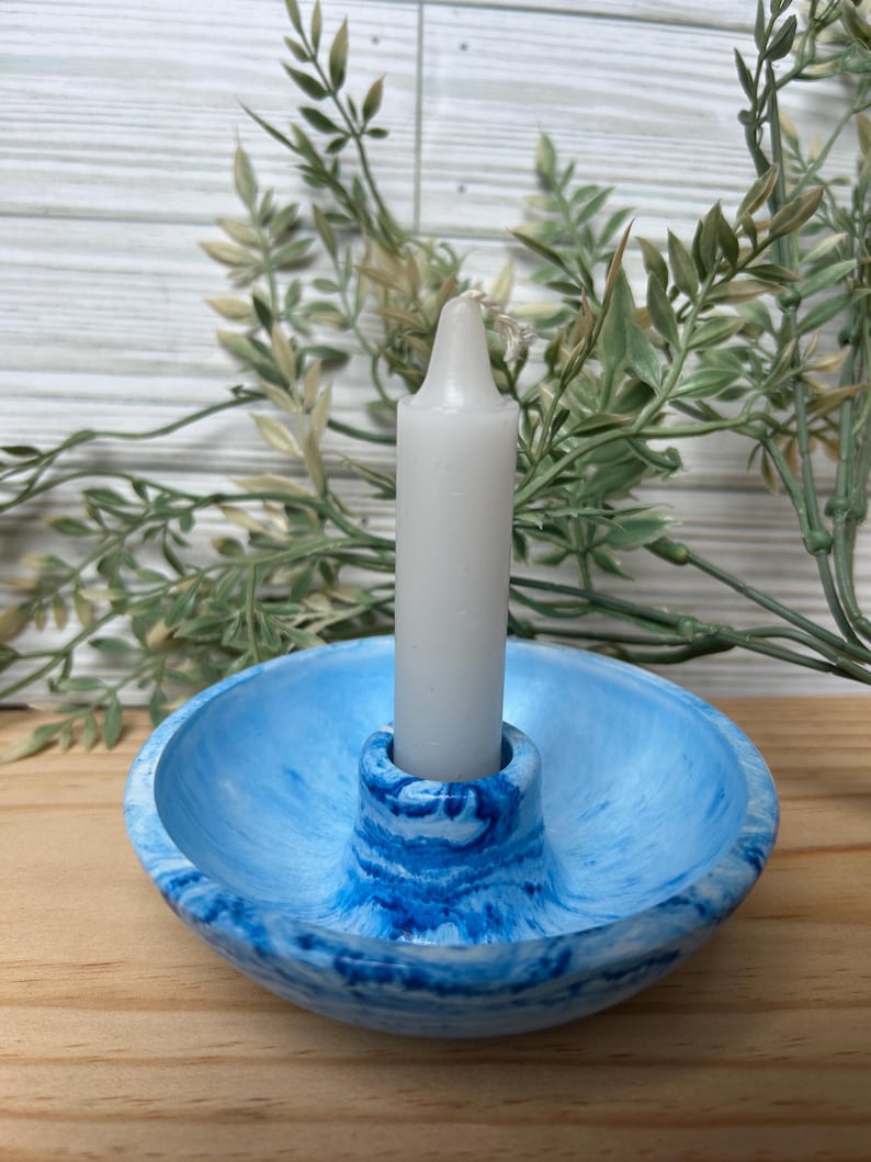 Op de afbeelding: Een blauw-witte gemarmerde kandelaar met een witte kaars. De kandelaar heeft een cirkelvormige basis en een centrale kolom om de kaars vast te houden. De kaars is wit en cilindrisch. Decoratieve woondecoratie.