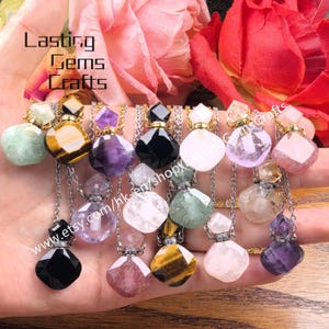 Puede incluir: Una colección de collares con colgantes de piedras preciosas en varios colores, incluyendo verde, amarillo, morado, negro y rosa. Cada collar presenta una pequeña botella de gema facetada con una cadena plateada. La imagen incluye el texto "Lasting Gems Crafts" y una dirección web.
