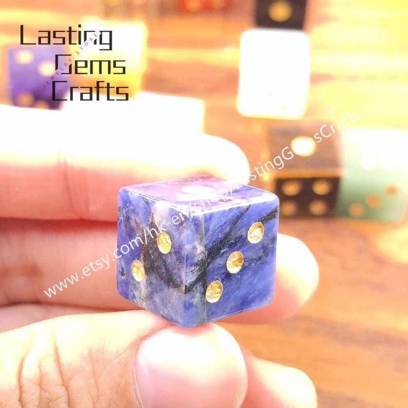 May include: A close-up of a blue and gold dice. The dice is made of a dark blue stone with gold-colored dots. The dice is being held by a person. The text "Lasting Gems Crafts" and a website address are visible.