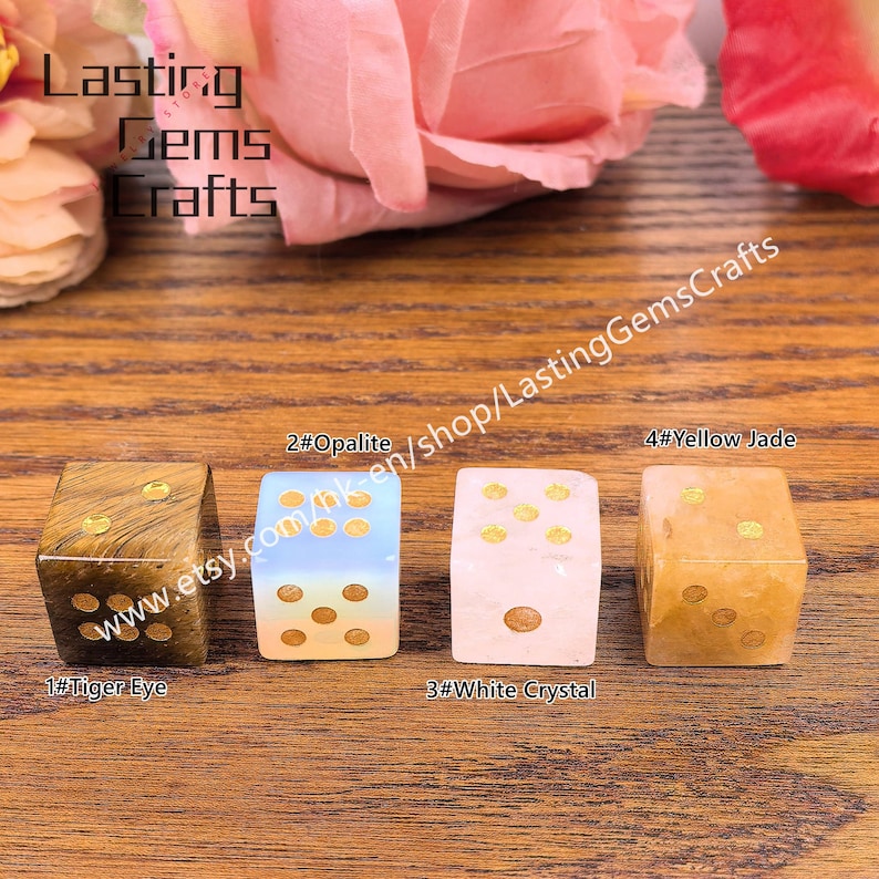 May include: Four gemstone dice: Tiger Eye, Opalite, White Crystal, and Yellow Jade. Each die features gold-colored dots. The dice are displayed on a wooden surface, with the shop name "Lasting Gems Crafts" visible.